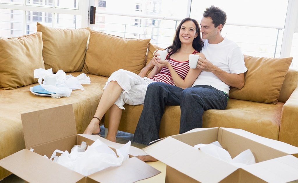 Couple relaxing with coffee by boxes in new home smiling